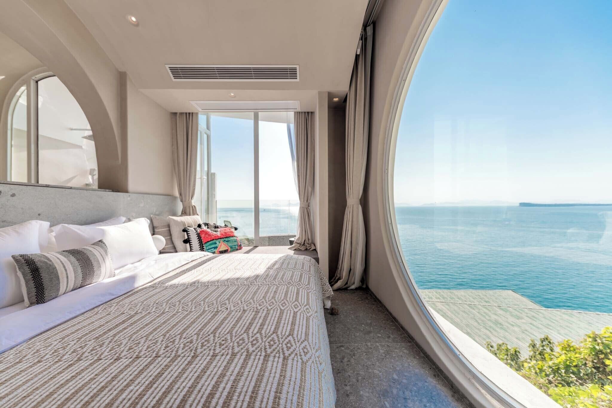 A modern bedroom with a large bed, a view of the sea, and a sliding door leading to a balcony.