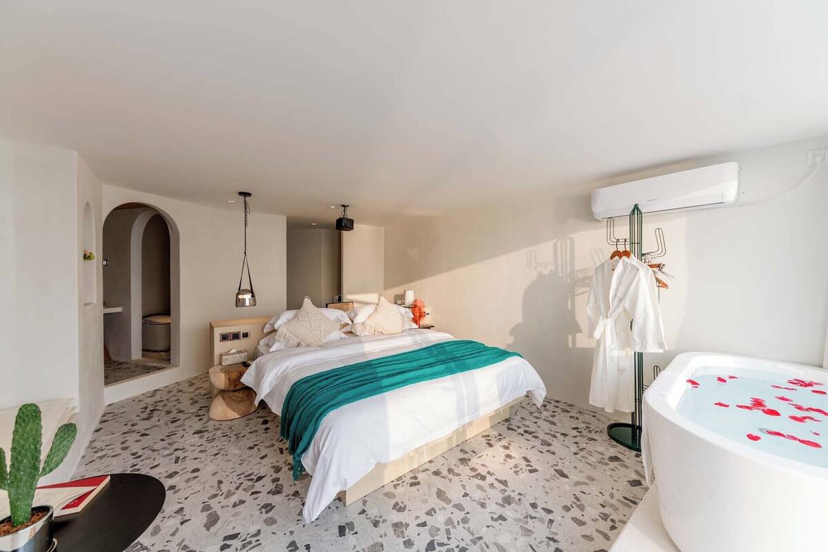 Une chambre à coucher moderne avec un lit, une grande fenêtre, un dressing et une salle de bain avec baignoire.