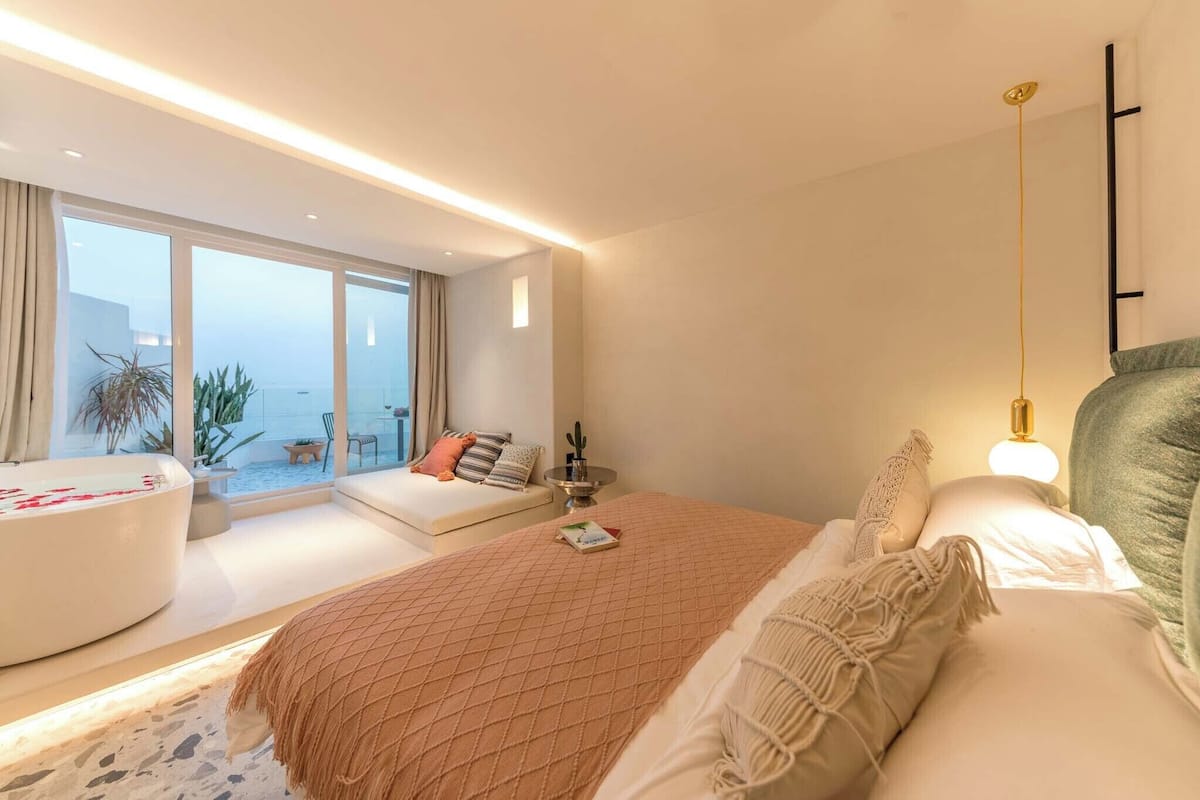 Une chambre moderne dotée d’un grand lit, d’un coin salon avec vue et d’un balcon agrémenté de plantes.