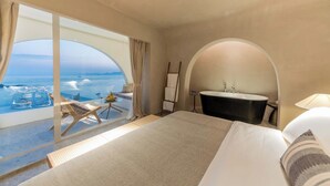 Une chambre d’hôtel avec un grand lit, une salle de bain avec baignoire et un balcon avec vue sur la mer.