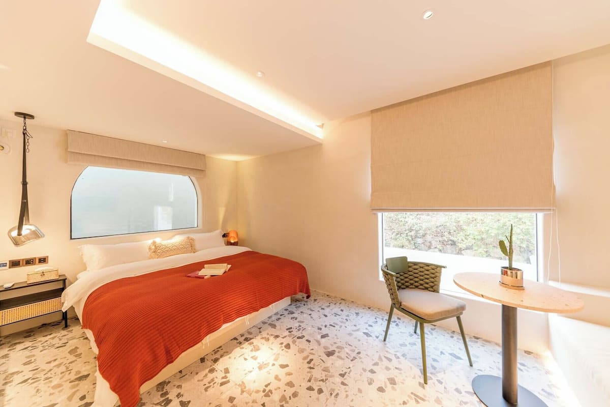 Une chambre moderne avec un grand lit, une petite table, une chaise et une fenêtre donnant sur un beau paysage.