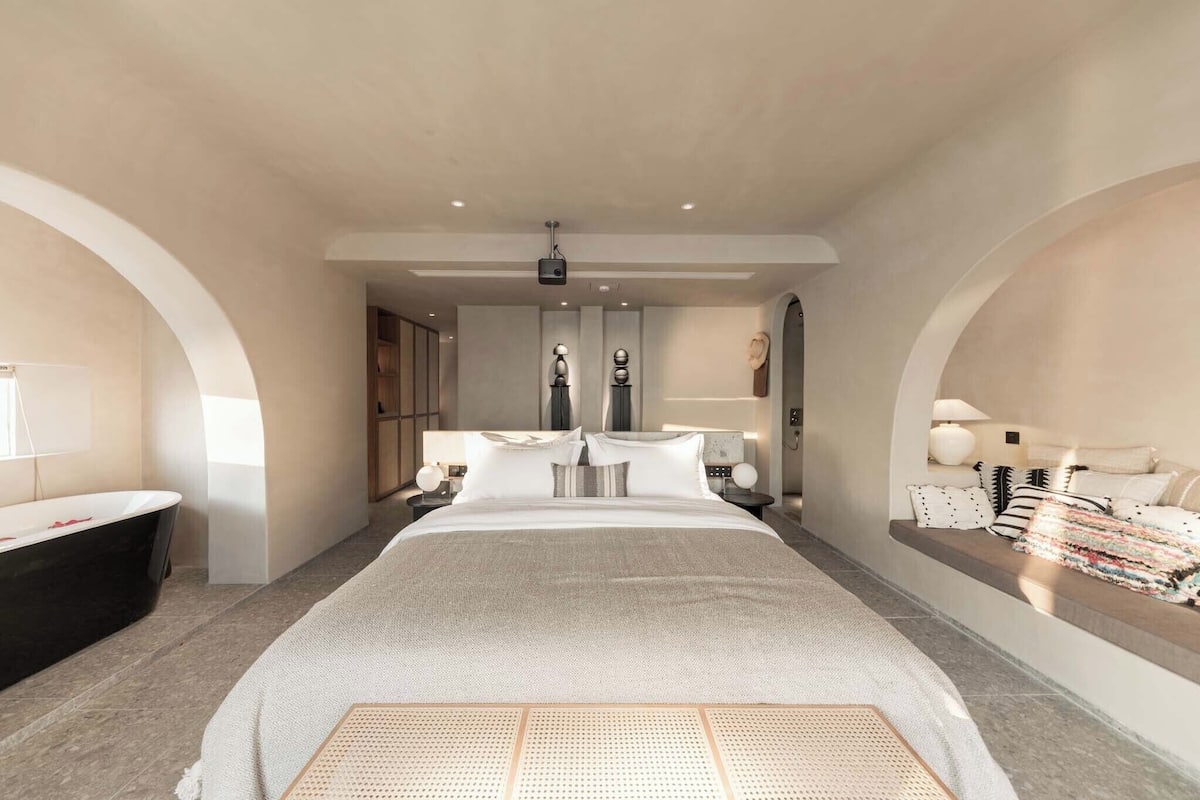 Une chambre moderne avec un grand lit, une baignoire et un coin salon agrémenté de coussins.