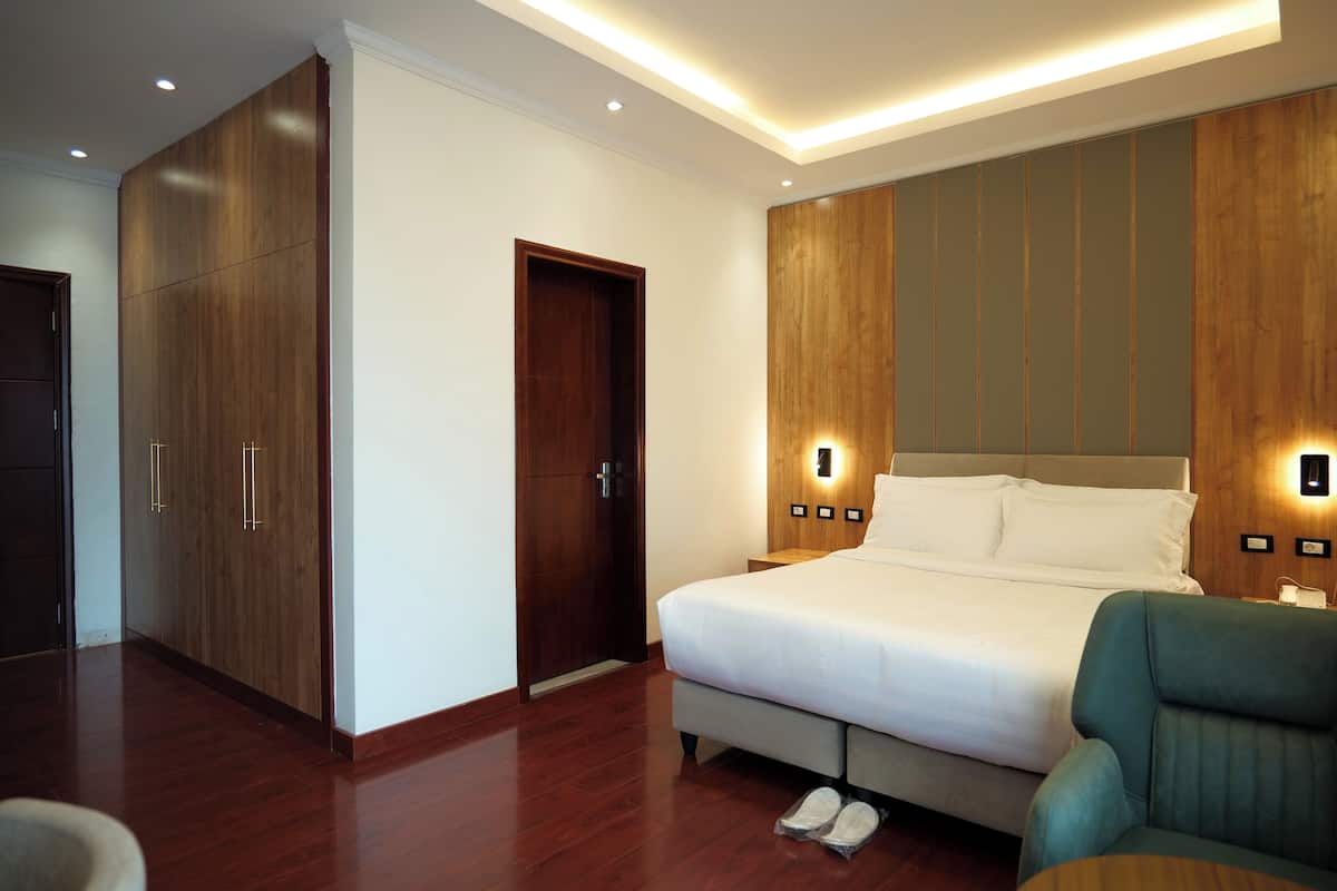 A modern hotel room with a large bed, wooden wardrobe, and built-in wall lighting.