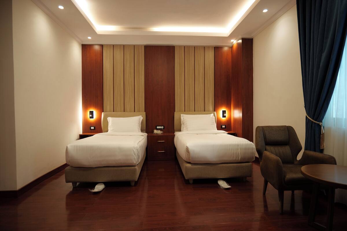 A hotel room with two beds, a small table, a chair, and a desk with a lamp.