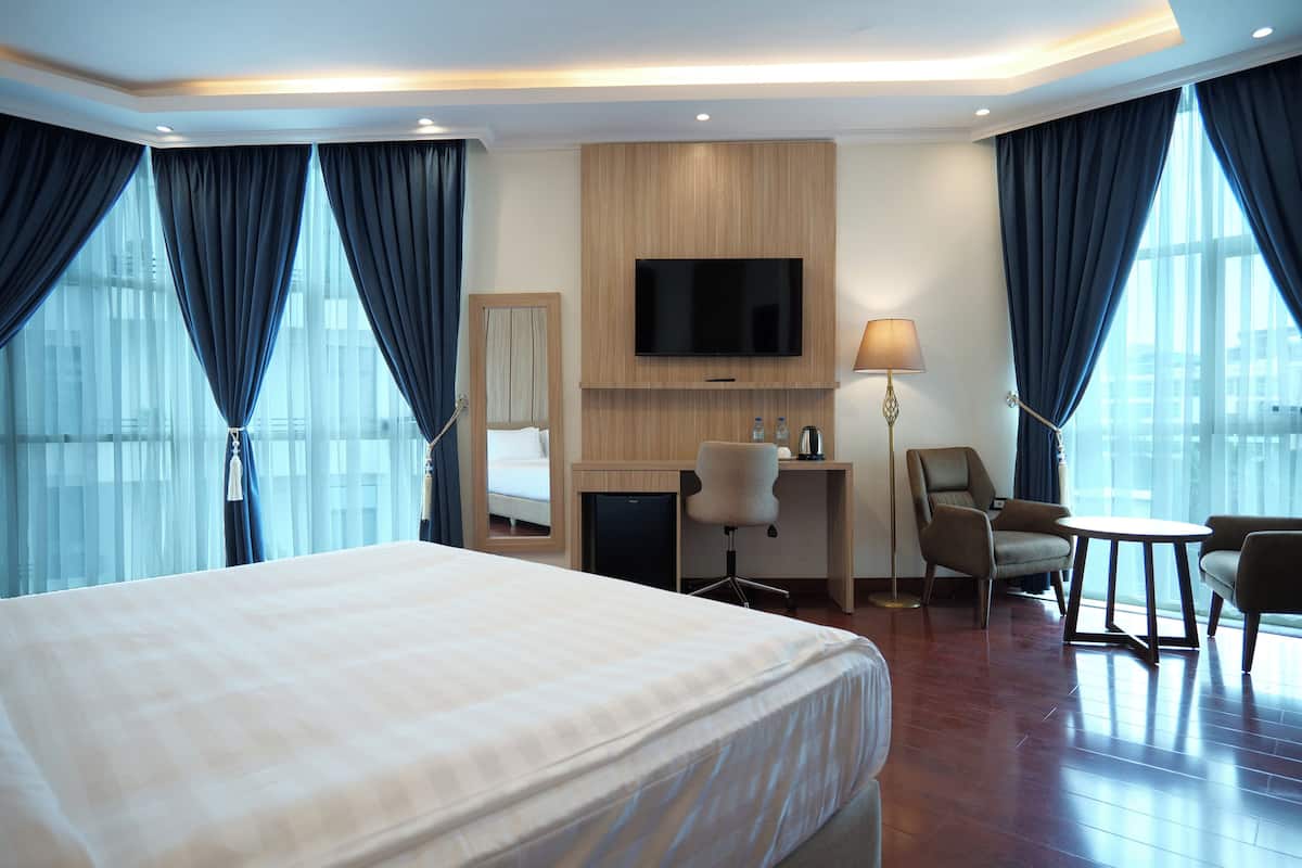 A hotel room with a large bed, a desk with a chair, a TV, and a lamp.