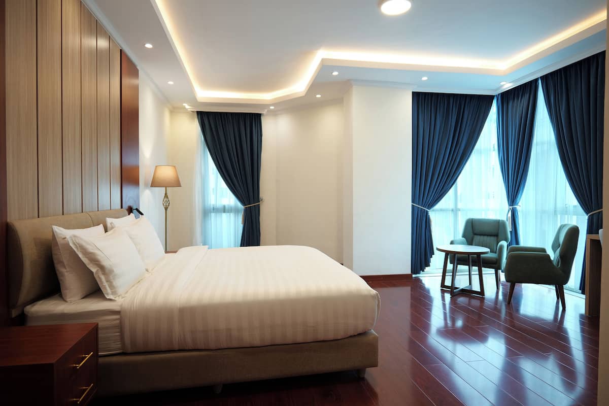 A hotel room with a large bed, two armchairs, a small table, and a lamp.
