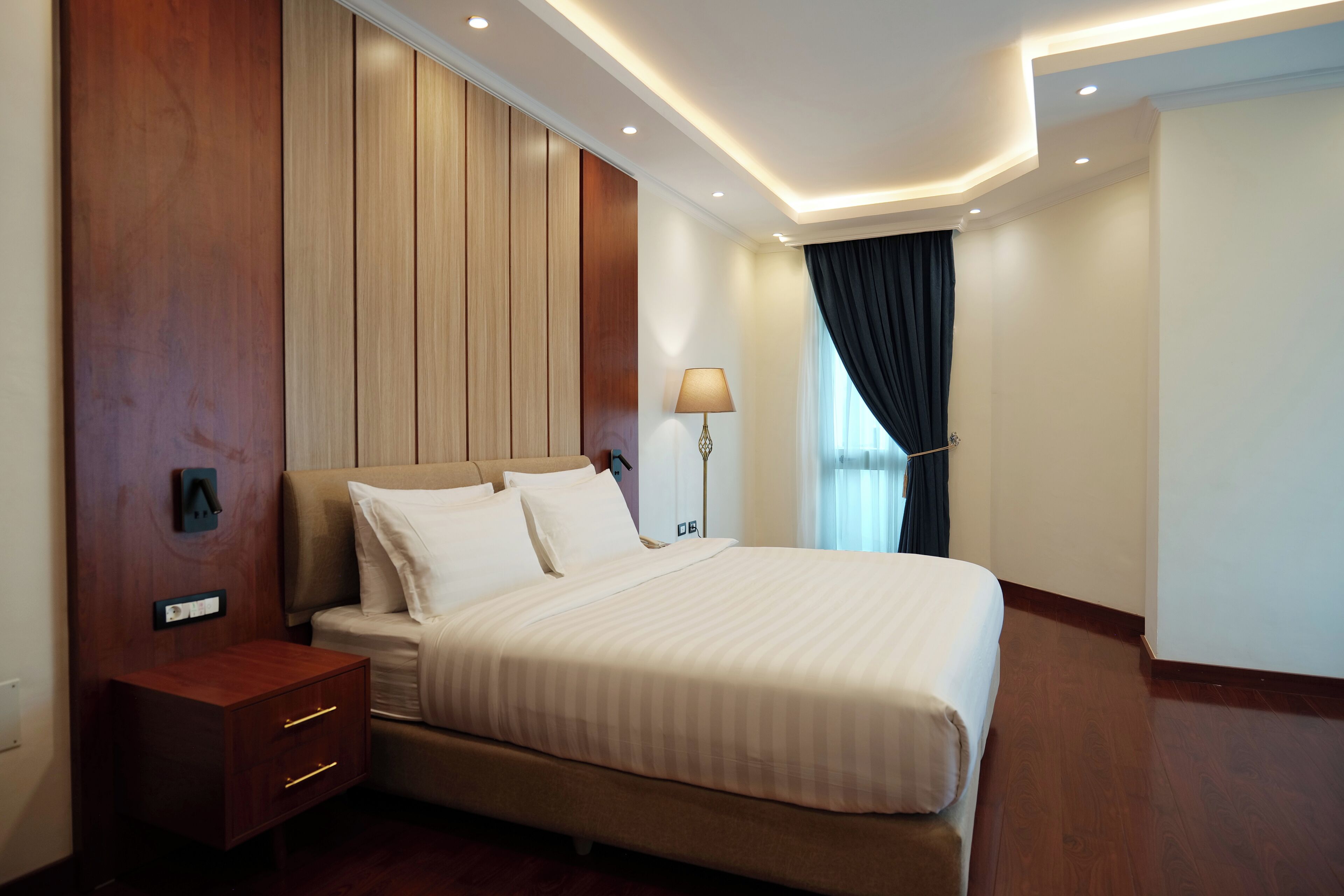 Una habitación de hotel con una cama grande, una mesita de noche, una lámpara y una ventana con cortinas.