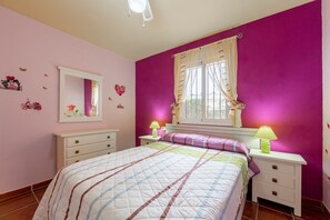 Une chambre à coucher comprenant un lit, deux tables de chevet, une fenêtre avec des rideaux, un miroir et des éléments de décoration murale.