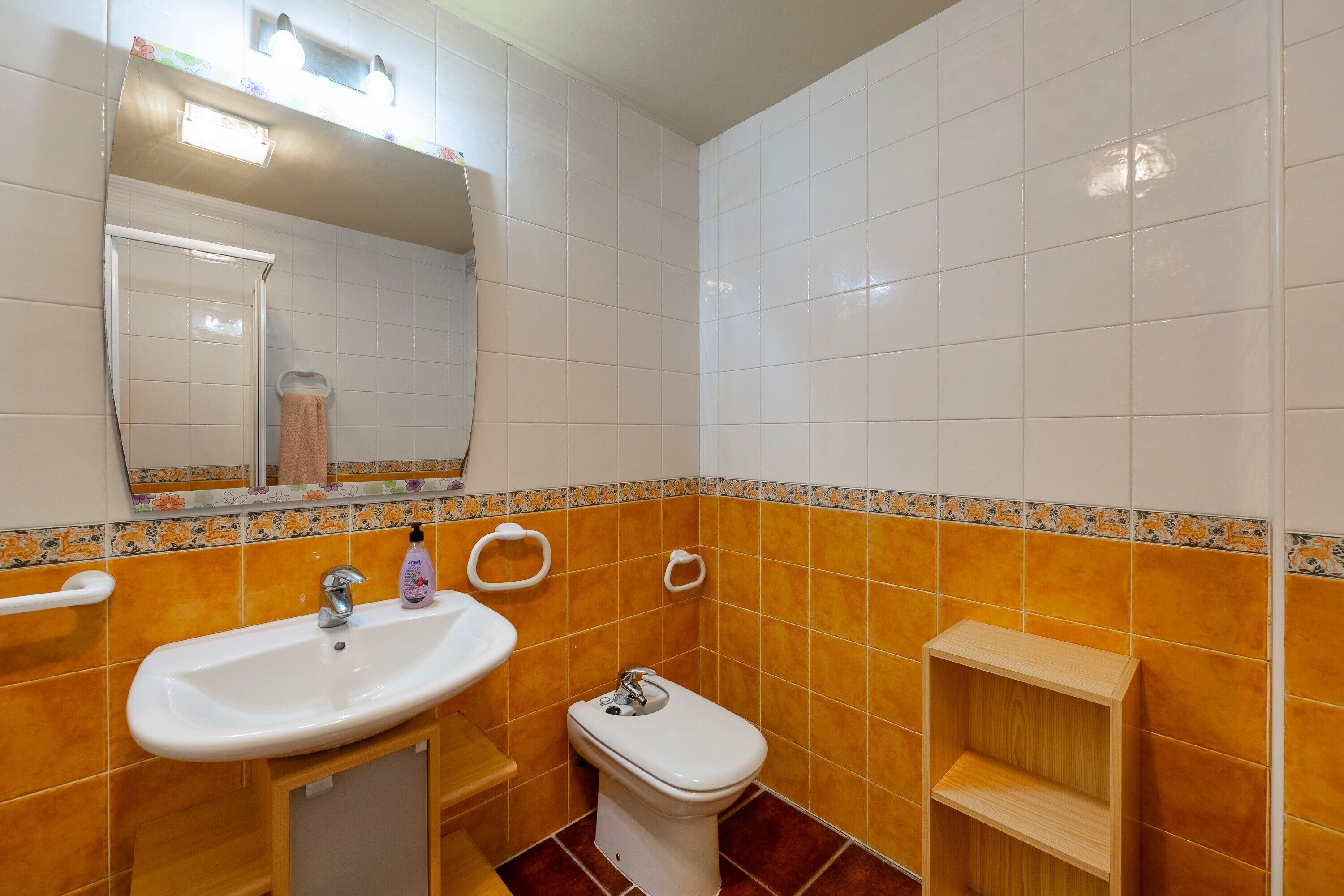 A bathroom with a sink, toilet, mirror, and a shelf.