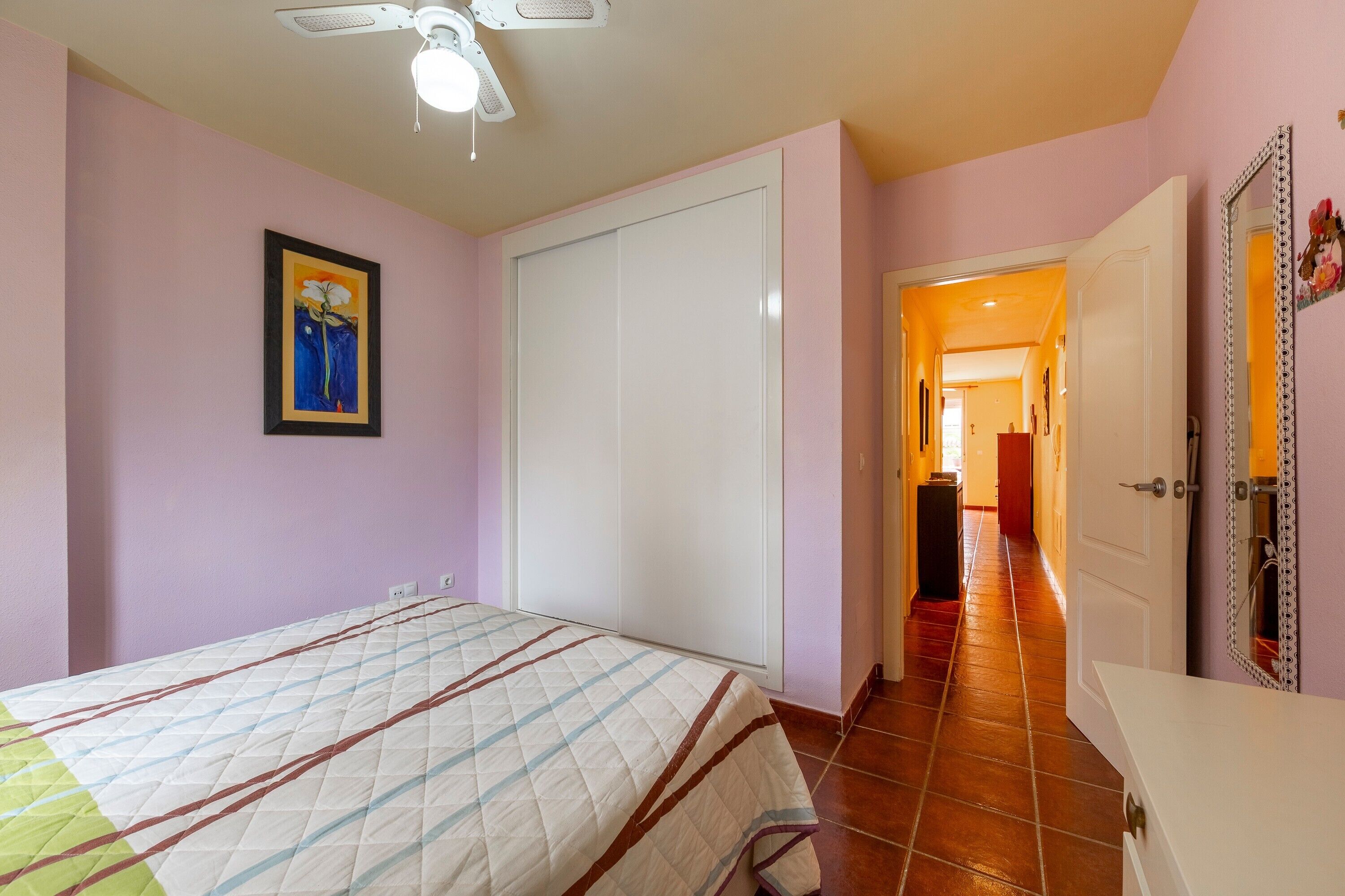 Ein Schlafzimmer mit einem Bett, einem Deckenventilator, einer Tür und einem Gang, der in einen anderen Raum führt.