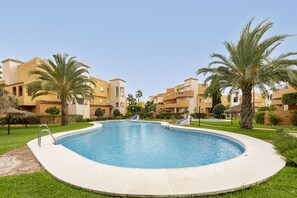 Une piscine entourée de palmiers et un bâtiment doté de balcons.