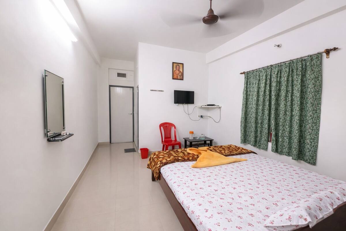 A bedroom with a bed, a television, a red chair, a small table, and a window with curtains.