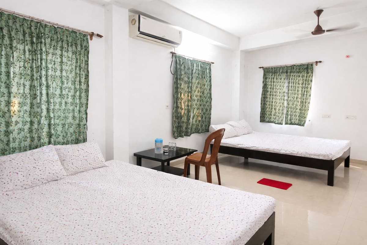 A hotel room with two beds, a chair, a small table, an air conditioning unit, and curtains.