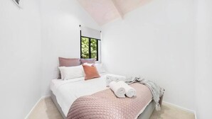 Une chambre moderne avec un grand lit, une fenêtre donnant sur un paysage verdoyant et un plafond avec des poutres apparentes.