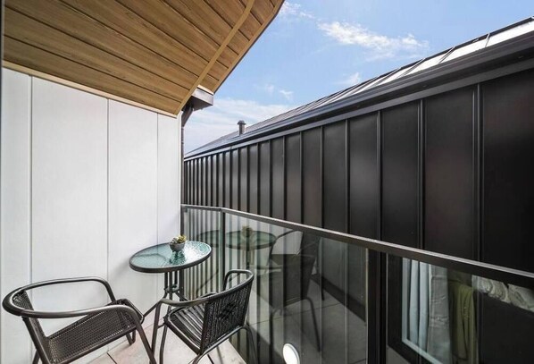 Un balcon doté d’une balustrade en verre, une petite table ronde et deux chaises.