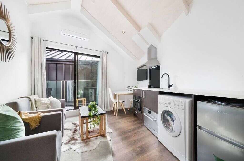 Ein kompakter Wohnbereich mit einer Couch, Esstisch und einer Küchenzeile inklusive Waschmaschine und Backofen.