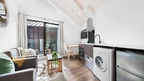 Un espace de vie compact comprenant un canapé, une table à manger et un coin cuisine équipé d’un lave-linge et d’un four.