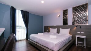 A modern hotel room with a large bed, a bedside table, a chair, and a view of the city through the window. - One Budget Hotel Chiangrai Soi Sawan (Chiang Rai)