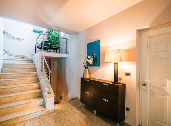 A staircase leading to an upper level with a glass railing, a dark wooden console table with a lamp, and a door to the right. - Villa Marid Opatija (Opatija)