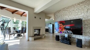 A spacious living area with a fireplace, a large flat-screen TV mounted on a stone wall, and a dining area with chairs and a table. - Villa Marid Opatija (Opatija)