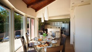 A dining area with a table set for four, a kitchen in the background, and a sliding glass door leading to an outdoor space. - Villa Marid Opatija (Opatija)
