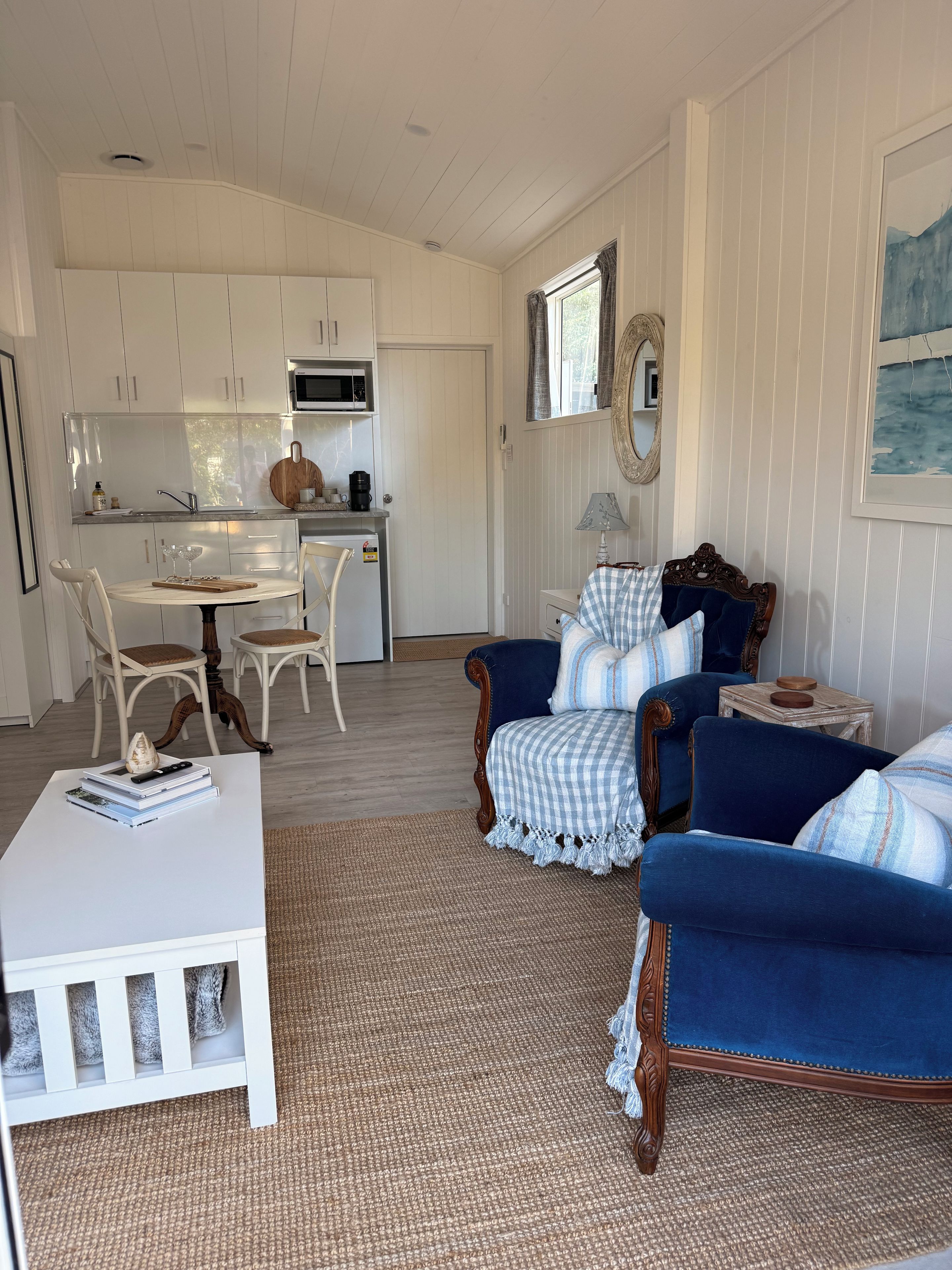 Ein Wohnzimmer mit einem weißen Couchtisch, blauen Sesseln, einem weißen Sofa und einem Essbereich mit weißen Stühlen und einem Holztisch.