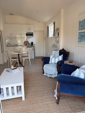 A living room with a white coffee table, blue armchairs, a white sofa, and a dining area with white chairs and a wooden table. - Hamptons style, studio retreat with light continental breakfast included (Strathalbyn)