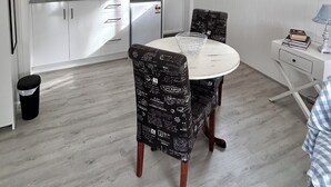 A compact kitchen with white cabinets, a microwave, and a sink. There is a dining table with chairs and a small side table with a lamp and books. - Hamptons style, studio retreat with light continental breakfast included (Strathalbyn)