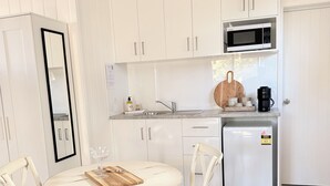 A kitchen with white cabinets, a microwave, and a coffee maker. There is a round table with chairs and a refrigerator. - Hamptons style, studio retreat with light continental breakfast included (Strathalbyn)