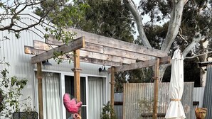 A rustic outdoor area with a wooden pergola, a rooster, a metal rooster sculpture, and a rustic fountain. - Hamptons style, studio retreat with light continental breakfast included (Strathalbyn)