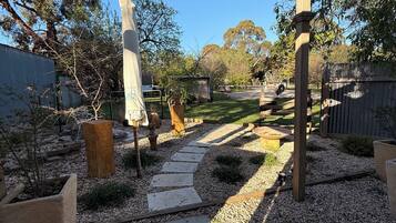 Un giardino con un vialetto in pietra, una pergola in legno e diverse piante in vaso.