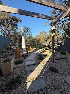 Ein Garten mit einem Kiesweg, einer Holzpergola und verschiedenen Kübelpflanzen.