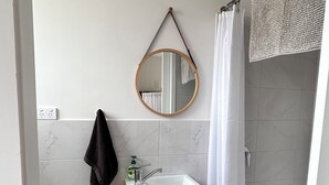 A bathroom with a wooden vanity, a mirror, a towel rack, a toilet paper holder, and a shower curtain. - Hamptons style, studio retreat with light continental breakfast included (Strathalbyn)