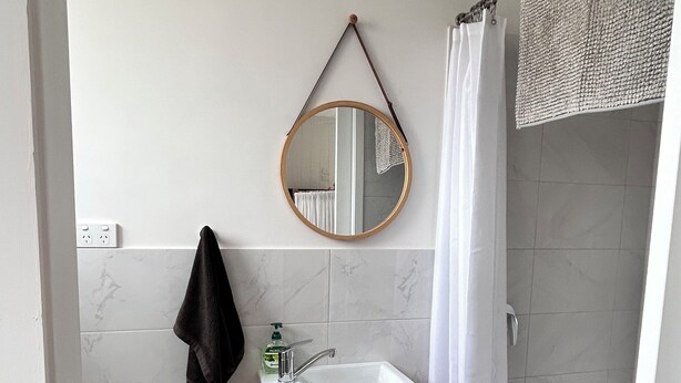 A bathroom with a wooden vanity, a mirror, a towel rack, a toilet paper holder, and a shower curtain. - Hamptons style, studio retreat with light continental breakfast included (Strathalbyn)