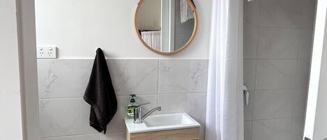 A bathroom with a wooden vanity, a mirror, a towel rack, a toilet paper holder, and a shower curtain.