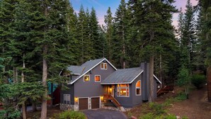 A two-story house with a dark gray exterior, a stone foundation, and a driveway leading to a wooden deck. - Forest Views, Hot Tub & Tahoe Donner Access | Alpenglow Chalet by AvantStay (Truckee)
