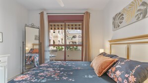 A bedroom with a bed, a mirror, a window with curtains, and a view of buildings outside.