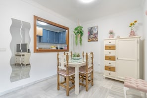 A dining area with a table and chairs, a cabinet, a hanging plant, and a painting on the wall.