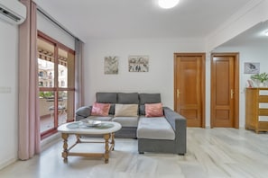 A living room with a grey sofa, a round wooden table, and a window with curtains.