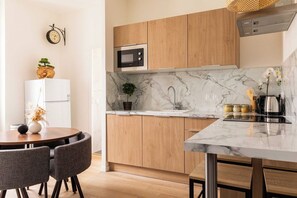 A modern kitchen with wooden cabinets, a built-in microwave, a marble countertop, and a dining area with a round table and chairs. - DIFY Apartment 2BR/4P - Paul Bert/Part-dieu (Lyon)
