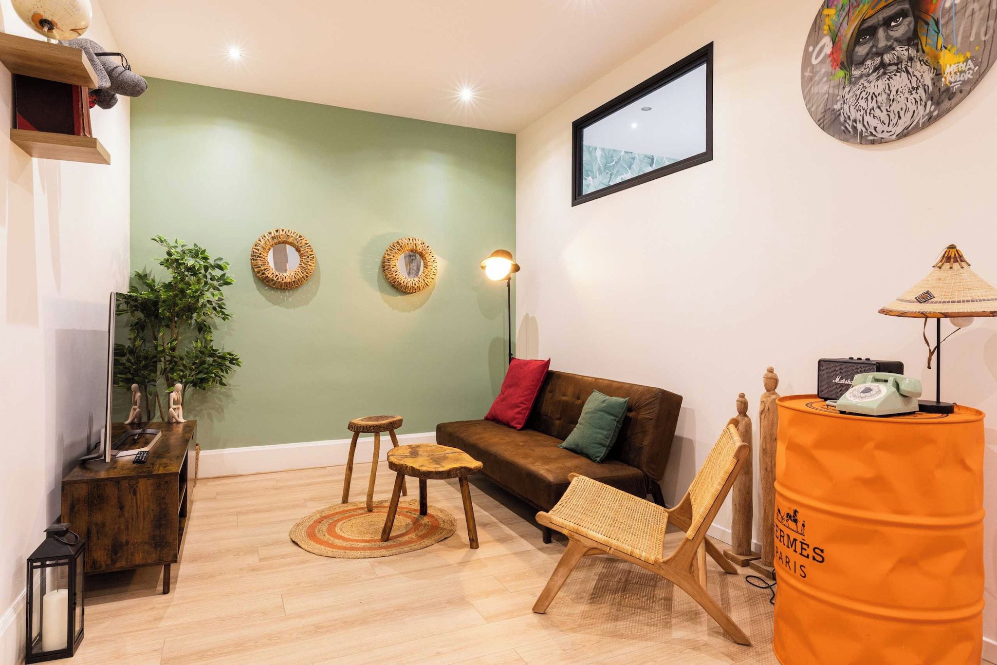 A living room with a green wall, a brown sofa, a wooden coffee table, a wicker chair, and a large orange barrel.