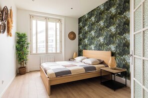 A bedroom with a wooden bed, a window, a potted plant, a woven wall hanging, and a textured wall. - DIFY Apartment 2BR/4P - Paul Bert/Part-dieu (Lyon)