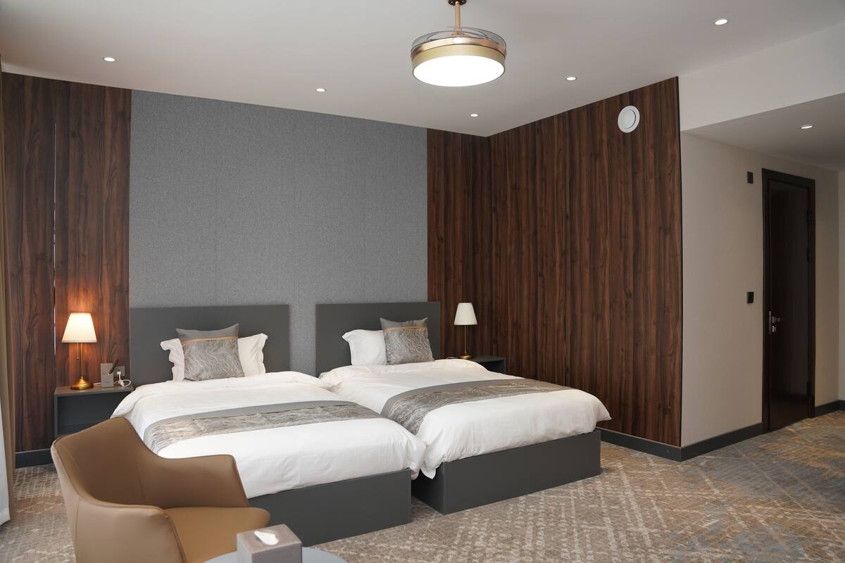 Een hotelkamer met twee bedden, een stoel, een bureau, een lamp en een plafondlamp.