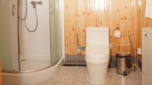 A bathroom with wooden walls, a shower, a toilet, and a trash bin. - Premium Bolor Resort Terelj (Ulaanbaatar)