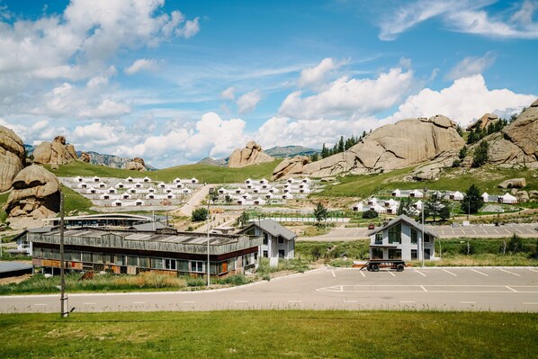 A modern hotel with a glass facade, situated in a mountainous area with large rock formations in the background.