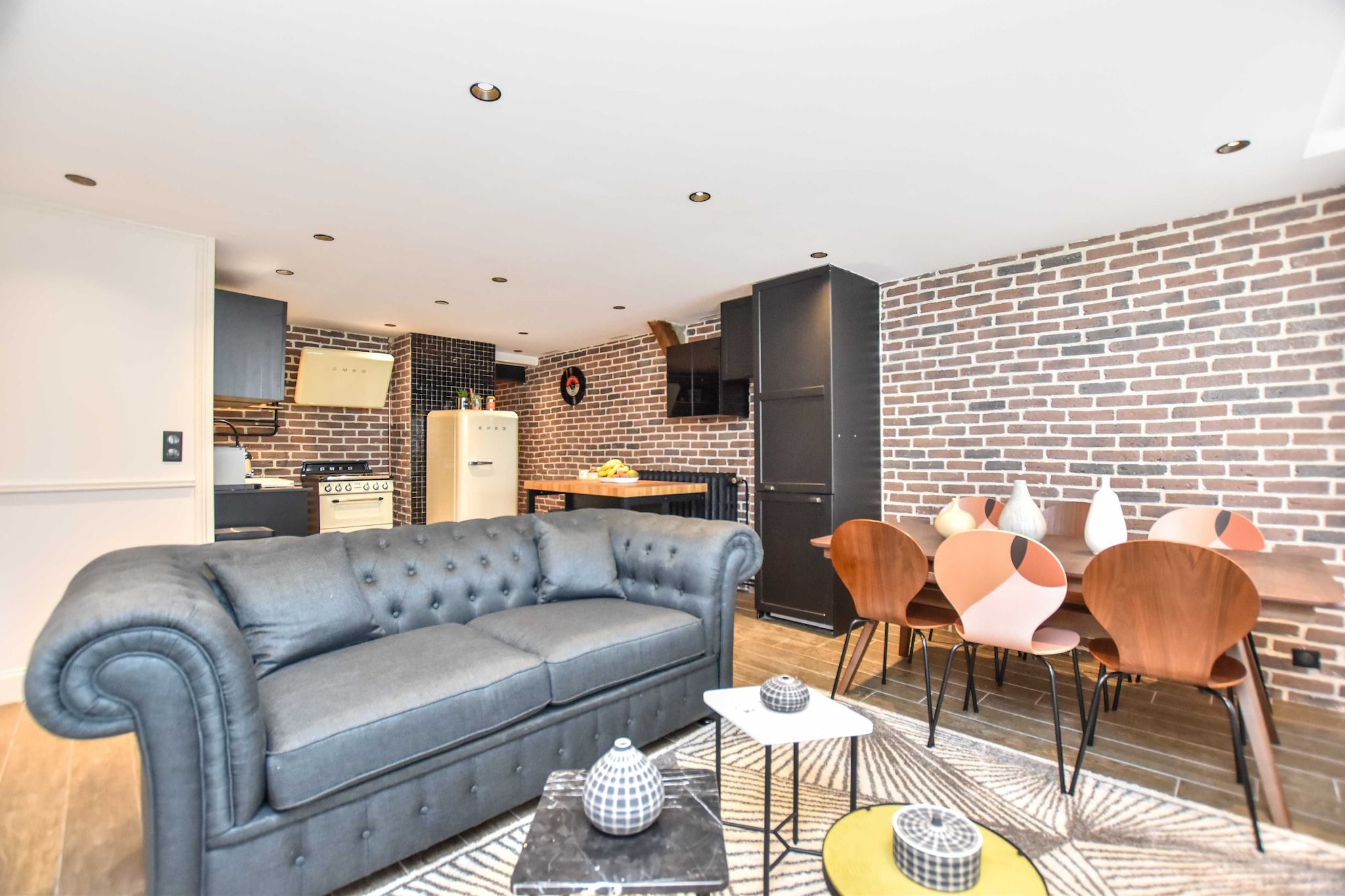 Ein modernes Wohnzimmer mit einem grauen Sofa, einer Essecke mit Holzkreisen und einer Küche mit Vintage-Geräten.
