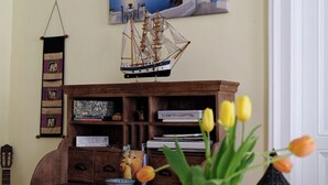 Un mueble de madera con cajones, una mesita con un jarrón de tulipanes y un modelo de barco en la pared.