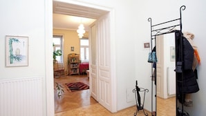 Un pasillo con un perchero, un radiador y una puerta que da a un salón.