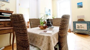 Comedor con sillas de mimbre, una mesa con mantel blanco y un aparador azul decorado con obras de arte.