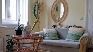 Un salón acogedor con un sofá gris, un espejo redondo y una silla de mimbre.